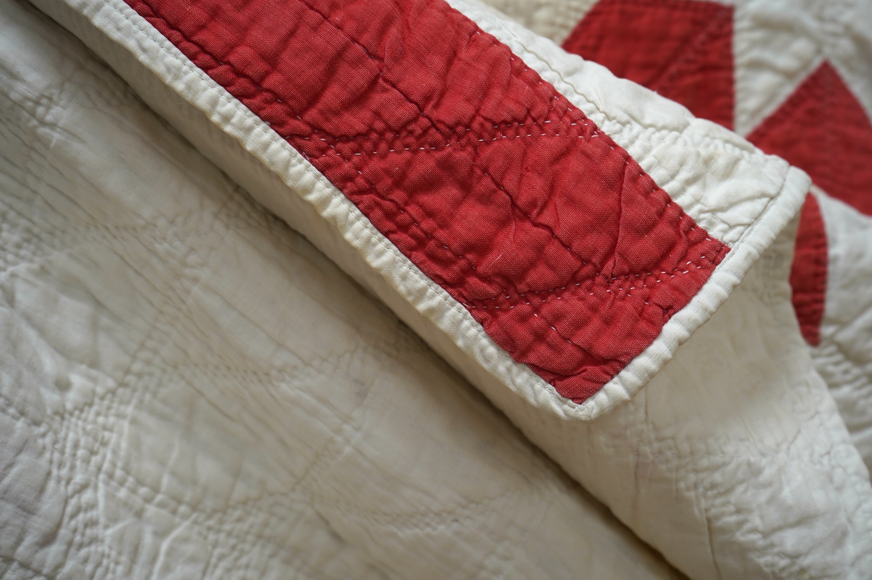 A late 19th century / early 20th century American ‘Star of Bethlehem’ quilt, worked on a plain light cream ground with red and yellow and beige patchworks forming a large double line star with a simple single red inner l